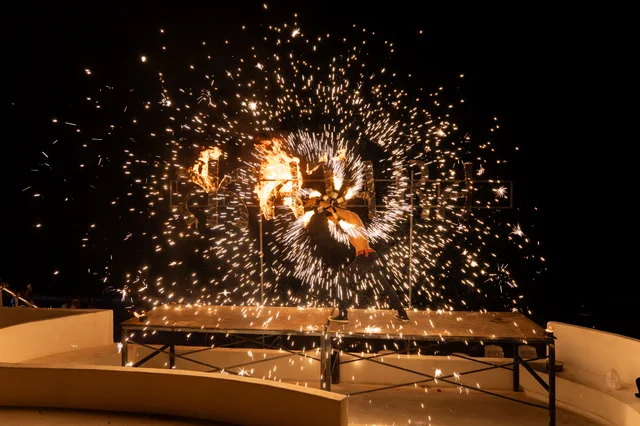 A fire performer surrounded by sparks on Katara’s beachfront stage at night.
