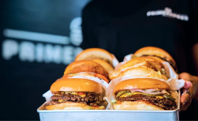 A tray of Prime Burger smash burgers held by a staff member